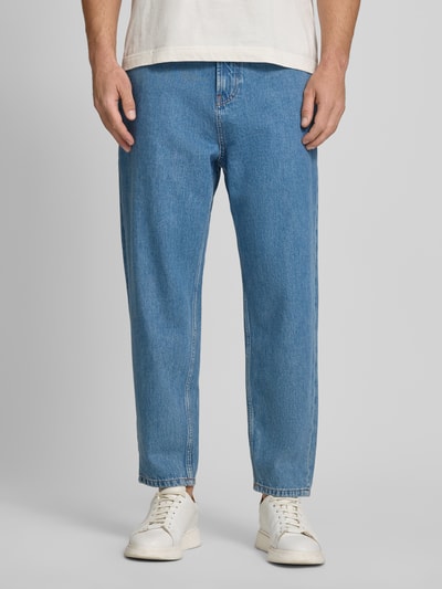 Männermodel trägt Wide Leg Tapered Fit Jeans aus Baumwoll-Ananas-Faser-Mix Modell 'ISAK' von Marc O'Polo Denim, Denim-Optik, Label-Patch, Nieten, Gürtelschlaufen, Bindegürtel, Kontrastnähte, seitliche Eingrifftaschen, angedeutete Münztasche, Gesäßtaschen, Knopf und verdeckter Reißverschluss, mittelblau, strukturierte Oberfläche, Ganzkörperansicht von vorne.