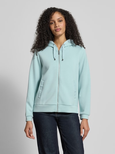 Modelka nosi Regular Fit Sweatjacke mit Viskose-Anteil von Tom Tailor, efekt: jednolity kolor, kaptur z tunelem, krój regular fit, zamek błyskawiczny, nadruk z logo na tunelu, długi rękaw, wykończenie z bocznymi rozcięciami, kieszenie listewkowe po bokach, jasnoniebieska, gładka faktura, widok całej sylwetki z przodu.