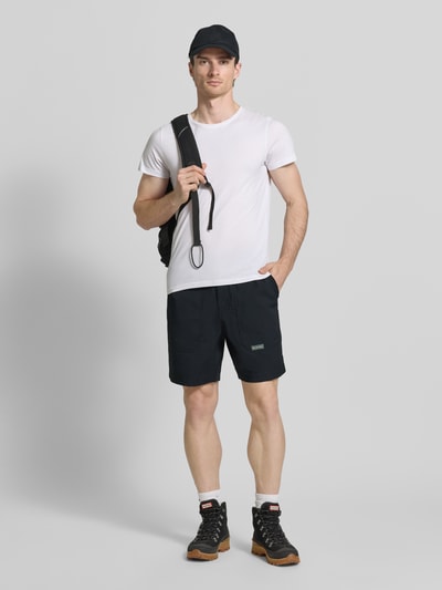 Männermodel trägt Regular Fit Shorts mit Logo-Patch Modell 'Landroamer' von COLUMBIA aus Elastischer-Material-Mix, Schwarz, Ganzkörperansicht von vorne. Shorts mit AufgesetzteTaschen, Elastischer Bund, Knopf-Reißverschluss, Bundweite 38 cm, Innenbeinlänge 18 cm.