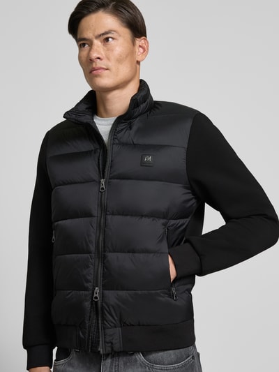 Männermodel trägt Jacke mit Label-Patch und Stehkragen von Antony Morato, Schwarz mit Zweiwege-Reißverschluss, Ganzkörperansicht von vorne.