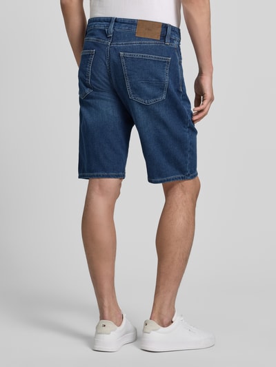 Männermodel trägt Regular Fit Jeansshorts aus Baumwoll-Mix von s.Oliver RED LABEL, blaue Denim-Optik, Label-Patch, Nieten, 5-Pocket-Design, Ganzkörperansicht Rückansicht.