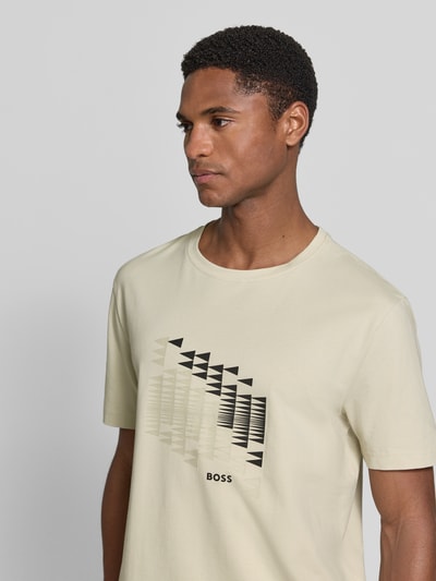 Männermodel trägt Relaxed Fit T-Shirt aus Baumwoll-Mix Modell 'TS_NETWORK FLAG' von BOSS Green, beiges Shirt mit schwarzem Grafikprint, Nahaufnahme Oberkörper.