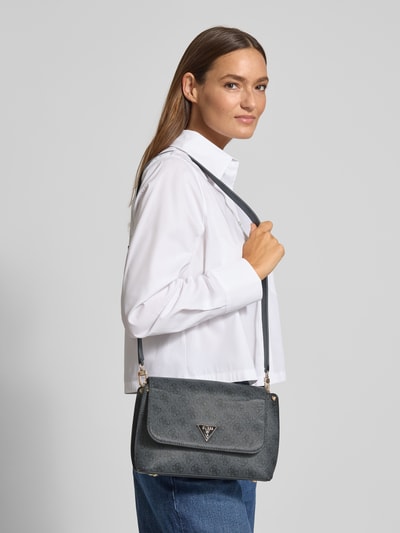 Kobiece modelka nosi torebkę Handtasche mit Logo-Muster und Label-Applikation od GUESS z szarym wzorem z logo, aplikacja z metką, klapka, zapięcie na magnes, pasek na ramię, model 'MERIDIAN II', szerokość w rozmiarze 1: 24 cm, długość w rozmiarze 1: 19 cm, głębokość w rozmiarze 1: 9 cm, długość paska na ramię w rozmiarze 1: 111 cm, widok całej sylwetki z przodu.
