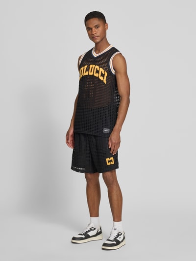 Männermodel trägt Straight Fit Shorts in Loch-Optik von COLUCCI, Schwarz mit Logo-Stitching, elastischer Tunnelzug, Ganzkörperansicht von vorne.