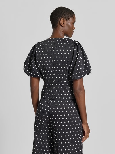 Frauenmodel trägt Slim Fit Bluse im Allover-Look Modell 'ANELA' von Neo Noir mit Puffärmeln, Hakenverschluss, schwarzen Grundton mit weißen Punkten, weiche Textur, Ganzkörperansicht Rückansicht. Damen Bluse von Neo Noir, Rundhalsausschnitt, Rückenlänge 48 cm, Ärmellänge 30 cm.