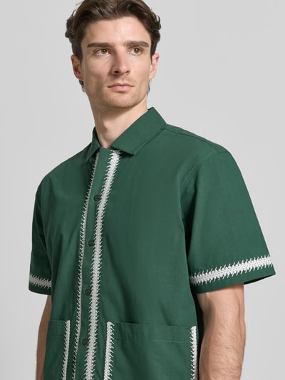 Männermodel trägt Regular Fit Freizeithemd mit aufgesetzten Taschen von WOODBIRD in grün mit Kentkraag, Stichdetails, Nahaufnahme Oberkörper.