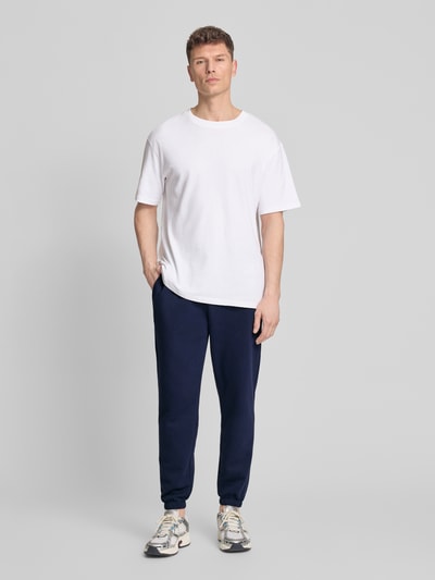 Männermodel trägt Sweatpants mit Logo und elastischem Bund von GAP aus Baumwoll-Mix in Dunkelblau, Regular-Fit, Ganzkörperansicht von vorne.