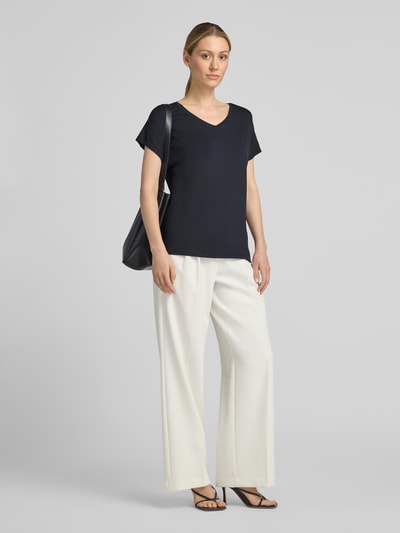 Frauenmodel trägt T-Shirt aus Viskose-Elasthan-Mix mit V-Ausschnitt von Christian Berg Woman, Relaxed Fit, dunkles Oberteil, helle Hose, Ganzkörperansicht von vorne.