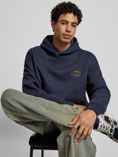 Männermodel trägt Oversized Hoodie mit Label-Stitching von PROHIBITED in Dunkelblau aus Baumwoll-Mix, Nahaufnahme Oberkörper.