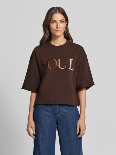 Frauenmodel trägt Cropped Boxy Fit Sweatshirt mit Label-Stitching von Smith and Soul in Dunkelbraun, Baumwoll-Elasthan-Mix, Rundhalsausschnitt, 1/2-Arm, kontrastfarbenes Logo auf der Front, gerade Form, Ganzkörperansicht von vorne.