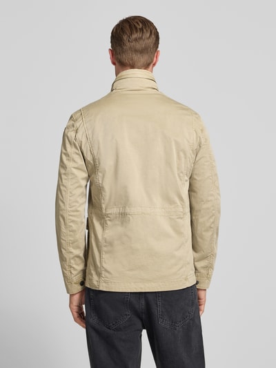 Męski model nosi kurtkę Jacke mit Stehkragen und Pattentaschen Modell 'Ashmont' von Blauer Usa, mieszanka bawełny i elastanu, krój regular fit, kieszenie z patką, jasny beż, długość tyłu w rozmiarze M: 72 cm, szerokość ramion w rozmiarze M: 40 cm, szerokość klatki piersiowej w rozmiarze M: 52 cm, długość rękawów w rozmiarze M: 63 cm, widok całej sylwetki z tyłu.