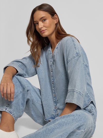 Vrouwenmodel draagt Loose Fit Jeansblouse uit katoen- en viscosemix Model 'VALERIA' van Vero Moda in denimlook, lichte wassing, 3/4-mouwen, V-hals, afgeronde rompzoom, detailopname bovenlichaam.