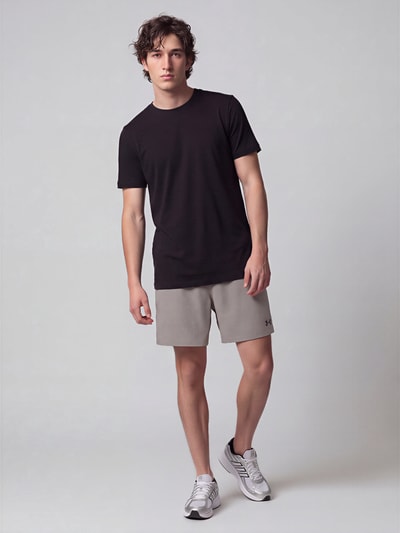Männermodel trägt Regular Fit Sportshorts mit Logo-Print von Under Armour in Hellgrau, glatte Textur, Ganzkörperansicht von vorne. Herren Sportshorts von Under Armour.