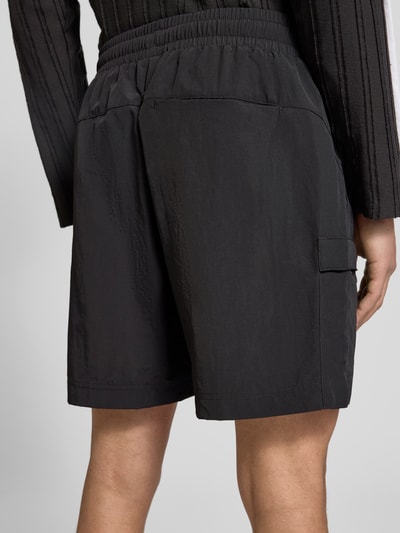 Männermodel trägt Relaxed Fit Shorts mit Label-Stitching von PUMA PERFORMANCE, schwarz, elastischer Bund, Cargotasche, Ganzkörperansicht Rückansicht.