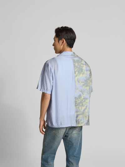 Männermodel trägt Relaxed Fit Freizeithemd aus Viskose-Mix von MAISON KITSUNÉ mit Brusttasche, Kurzärmelig, Rückenlänge 73 cm, Schulterbreite 55 cm, Ärmellänge 28 cm, helle Farben, rechte Hälfte mit abstraktem Muster, Ganzkörperansicht Rückansicht.