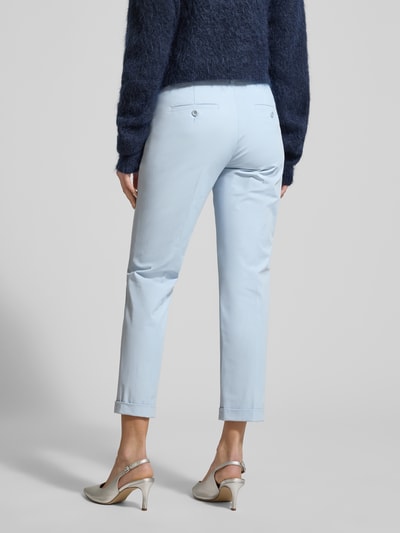 Frauenmodel trägt Chino aus Techno Cotton Superstretch Modell 'UTE' von Raffaello Rossi in Hellblau, elastischer Material-Mix, Straight Fit, verkürzte Passform, Knopf- und Reißverschluss, Eingriff- und Gesäßtaschen, Bügelfalten, fixierte Beinumschläge, Gürtelschlaufen, Ganzkörperansicht Rückansicht.