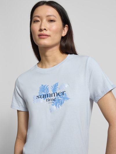 Frauenmodel trägt Regular Fit T-Shirt aus reiner Baumwolle von Tom Tailor in Hellblau, unifarben mit Motiv- und Label-Print, Jerseytextur, Nahaufnahme Oberkörper.