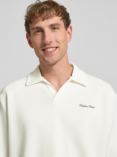 Männermodel trägt Regular Fit Poloshirt mit Logo Modell 'Eddie' von Redefined Rebel aus Baumwoll-Mix in Creme, Nahaufnahme Oberkörper. Rückenlänge bei Größe M: 73 cm, V-Ausschnitt.