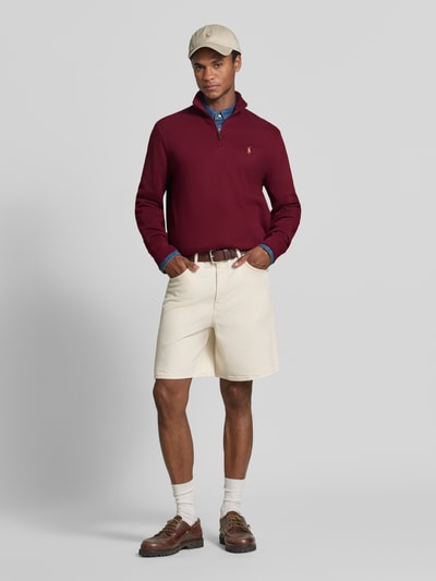 Mannenmodel draagt Relaxed Fit schipperstrui van puur katoen van Polo Ralph Lauren in bordeaux, crèmekleurige short, ganzekopsvooraanzicht.