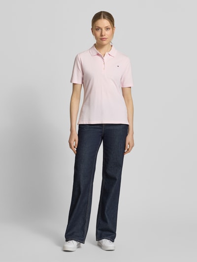 Vrouwenmodel draagt Regular Fit Poloshirts aus Baumwoll-Mix van Tommy Hilfiger in effen lichtroze piqué met logo-stitching, korte knoopsluiting, polokraag, korte mouwen en V-hals, materiaalverwerking katoenmix, voorkant full-body opname.