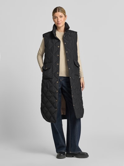 Vrouwenmodel draagt zwarte lange bodywarmer in stiksels van FREE/QUENT, regular fit, opstaande kraag, opgestikte zakken, knoopsluiting, mouwloos design, Model 'Olga', ruglengte maat S 113 cm, schouderbreedte 44 cm, borstwijdte 54 cm, geheel lichaamsaanzicht van voren.