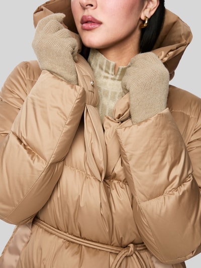 Frauenmodel trägt Steppmantel mit Bindegürtel von Marc Cain in Beige, wattierte Oberfläche, Kapuze, verdeckter Reißverschluss, Nahaufnahme Oberkörper.