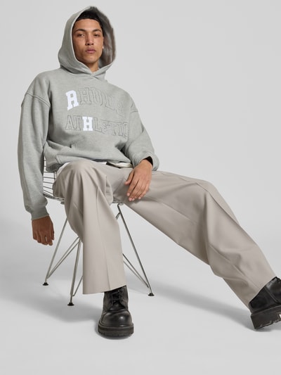 Männermodel trägt Oversized Hoodie mit Logo-Print von RHUDE aus Baumwoll-Mix, Känguru-Tasche, elastische Abschlüsse, Oversized-Fit, Ganzkörperansicht von vorne.