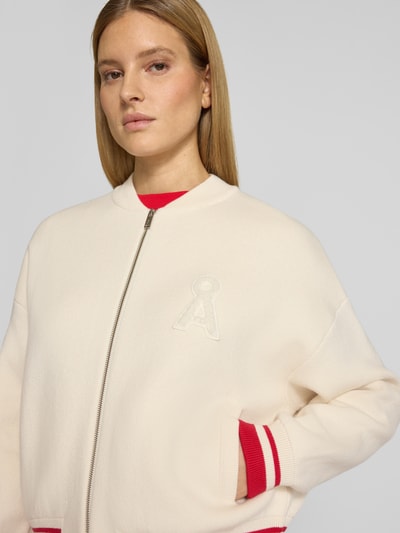 Frauenmodel trägt Oversized Bomberjacke aus Baumwoll-Mix mit Woll-Anteil Modell 'ICONIC A' von Armedangels, cremefarben, unifarben, mit Logo-Stitching und College-Kragen, Rippstrick an Ärmeln und Saum, Nahaufnahme Oberkörper.
