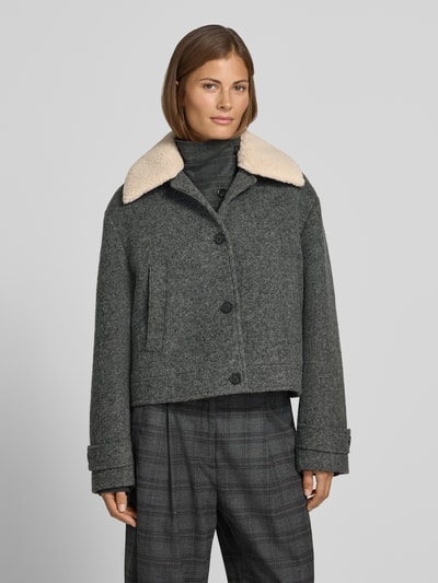 Frauenmodel trägt Jacke mit Kentkragen und Eingrifftaschen von Style Icon Collection in Grau, sichtbare Knopfleiste, Ganzkörperansicht von vorne. Gerader Schnitt, seitliche Eingrifftaschen, Ärmelriegel mit Knopf, Struktur aus weichem Wollstoff, dezente Karomuster-Hose, Kontext: Rückenlänge 54 cm, Schulterbreite 52 cm, Brustweite 50 cm, Ärmellänge 60 cm.