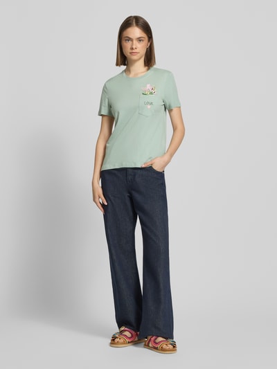 Frauenmodel trägt Damen T-Shirt von Only, Modell 'Regular Fit T-Shirt aus reiner Bio-Baumwolle Modell POLLY', Optik: Unifarben, Regular-Fit, Statement-Print-Applikation und Motiv-Stitching, Rundhals, Kurzarm, Brusttasche mit Innenseite mit versteckter Botschaft, Materialverarbeitung: Jersey aus reiner Bio-Baumwolle, sanftes Mintgrün und glatte Textur, Ganzkörperansicht von vorne.