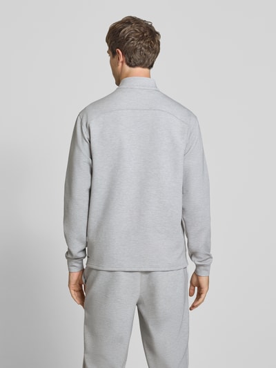 Męski model nosi bluzę rozpinaną z stójką i logo 'Sweatjacke mit Stehkragen und Logo' od PUMA PERFORMANCE, mieszanka materiałów z dodatkiem lyocellu, krój regular fit, szara, zamek błyskawiczny, długość tyłu w rozmiarze M 71 cm, długość rękawów 70 cm, widok całej sylwetki od tyłu.