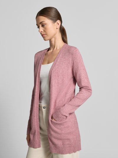 Frauenmodel trägt Strickjacke aus Viskose-Mix von VILA in Rosa mit taillierter Passform, seitlichen Eingrifftaschen, gerippten Abschlüssen, Rückenlänge 81 cm, Ärmellänge 68 cm, Ganzkörperansicht von vorne.