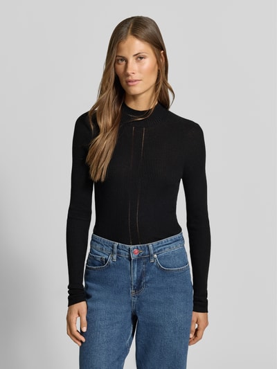 Frauenmodel trägt Slim Fit Pullover mit Woll-Anteil von MYON, schwarzer Material-Mix, Stehkragen, Lochmuster, Jeans, Ganzkörperansicht von vorne.