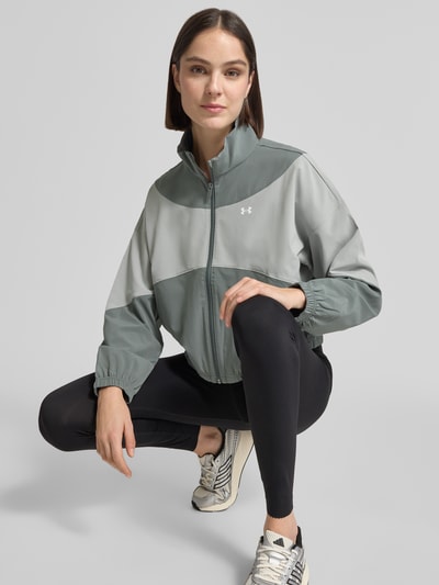Frauenmodel trägt Trainingsjacke mit Stehkragen und Eingrifftaschen von Under Armour in Grau mit Logo, Regular-Fit, Ganzkörperansicht von vorne. Rückenlänge bei Größe S: 60 cm, Schulterbreite bei Größe S: 62 cm, Brustweite bei Größe S: 57 cm, Ärmellänge bei Größe S: 50 cm.