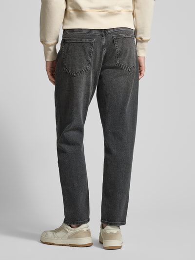 Männermodel trägt Tapered-Fit Herren Jeans aus Bio-Baumwoll-Mix Modell 'MAAKX' von Armedangels in dunkler Denim-Optik, Ganzkörperansicht Rückansicht. Passform: Relaxed Tapered-Fit, Mid Waist, Label-Patch, Gürtelschlaufen, 5-Pocket-Design, Verschluss: Knopf und Reißverschluss.