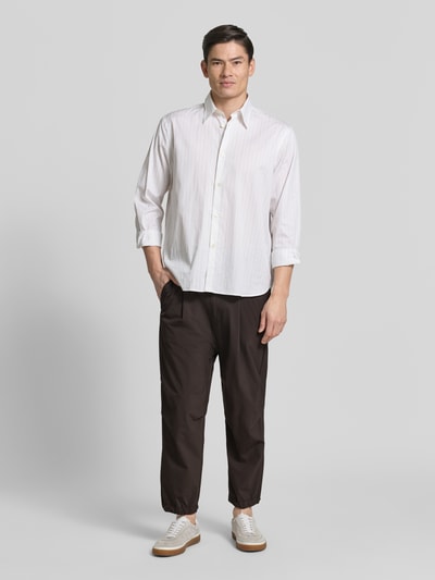 Männermodel trägt Relaxed Fit Hose mit Bundfalten Modell 'Lirog' von Drykorn aus Elastischer-Material-Mix in Dunkelbraun, Eingriff- und Gesäßtaschen, Knopf- und Reißverschluss, Bundweite 41 cm, Innenbeinlänge 62 cm, Ganzkörperansicht von vorne.