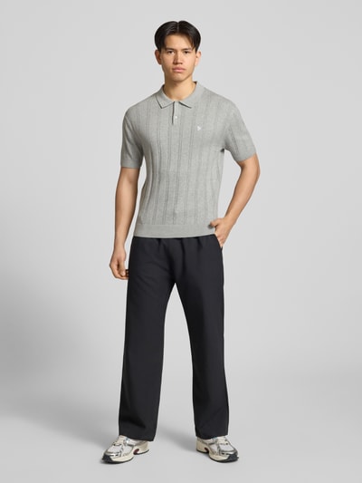 Männermodel trägt Slim Fit Strick-Poloshirt mit Label-Stitching von REVIEW in Grau mit Zopfmuster, Reine Baumwolle, Ganzkörperansicht von vorne.