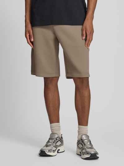 Männermodel trägt Bermudas mit Reißverschlusstaschen von EA7 Emporio Armani, Material-Mix mit Viskose-Anteil, Regular-Fit, Bundweite 41 cm, Innenbeinlänge 30 cm, Beige, glatte Textur, Ganzkörperansicht von vorne.