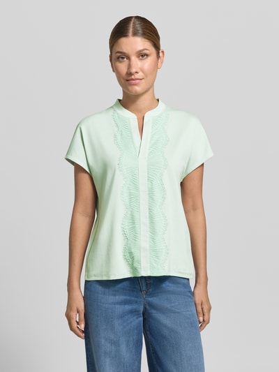 Frauenmodel trägt Regular Fit Bluse aus Baumwoll-Mix mit Spitzenbesatz von Marc Cain in Mint, Serafino-Ausschnitt, kurzärmelig, Ganzkörperansicht von vorne.