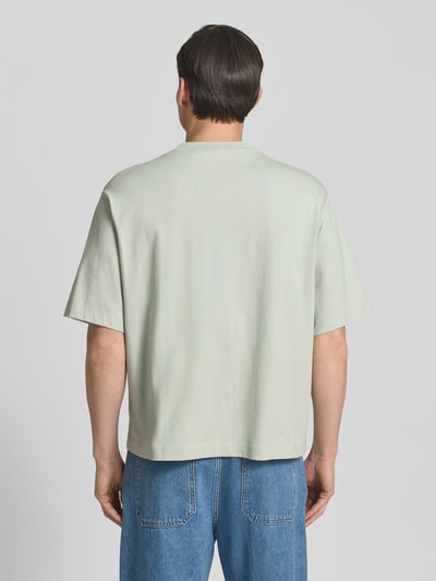 Männermodel trägt Relaxed Fit T-Shirt aus reiner Baumwolle Modell 'BOXYNORMAN GRAPHIC' von SELECTED HOMME, Hellgrün, Ganzkörperansicht Rückansicht