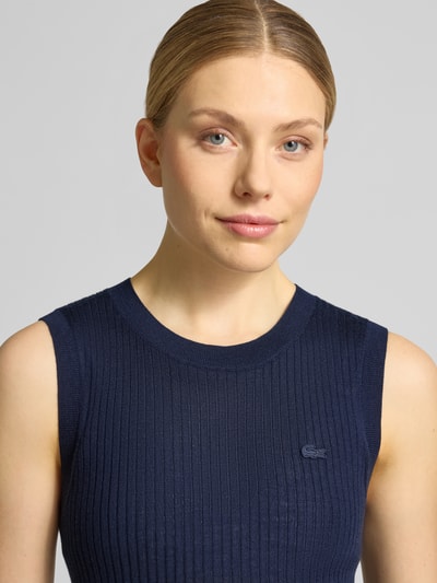 Frauenmodel trägt Slim Fit Pullunder aus reiner Wolle von Lacoste in Strickoptik mit gestreifter Struktur und Logo-Detail, Nahaufnahme Oberkörper.