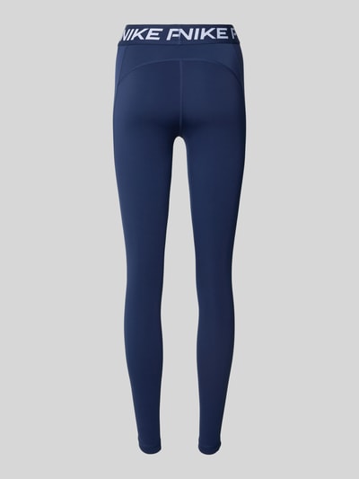 Männermodel trägt Slim Fit Leggins mit Logo-Print von NIKE TRAINING, elastyczna mieszanka materiałów, krój slim fit, nadruk z logo, elastyczny pas, kolor granatowy, struktura gładka, Ganzkörperansicht Rückansicht.