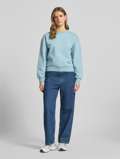 Frauenmodel trägt Sweatshirt mit Logo-Stitching Modell 'CASEY' von Carhartt Work In Progress in Hellblau, Reine Baumwolle, Loose-Fit, Rundhalsausschnitt, überschnittene Schultern, glatte Struktur, Ganzkörperansicht von vorne.