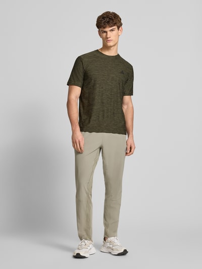 Männermodel trägt T-Shirt mit Label-Print von adidas Training in Olivgrün, Regular Fit, Material-Mix mit Stretch, Ganzkörperansicht von vorne.
