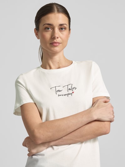 Vrouwenmodel draagt Regular Fit T-Shirt uit bio-katoenmix van Tom Tailor, effen ontwerp, ronde hals, korte mouwen, labeltekst, bovenlichaam close-up.