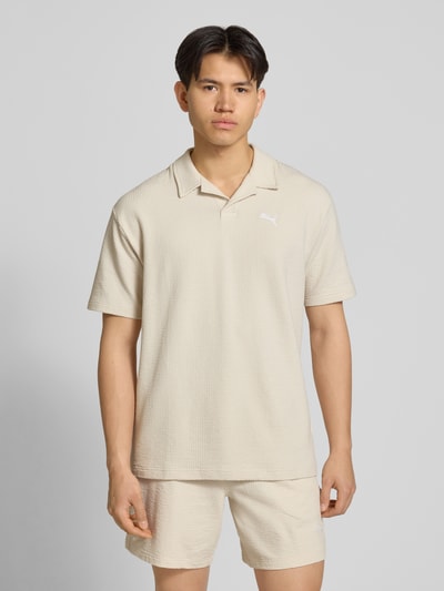 Männermodel trägt Regular Fit T-Shirt mit Logo-Stitching von PUMA PERFORMANCE, beige, Strukturmuster, Reverskragen, Nahaufnahme Oberkörper.