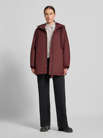 Frauenmodel trägt Relaxed Fit Mantel mit Kapuze Modell 'PURE' von g-lab in Dunkelrot, strukturierte Oberfläche, Ganzkörperansicht von vorne. Rückenlänge 69 cm, Schulterbreite 45 cm, Brustweite 88 cm, Ärmellänge 60 cm, Tunnelzug und Eingrifftaschen.
