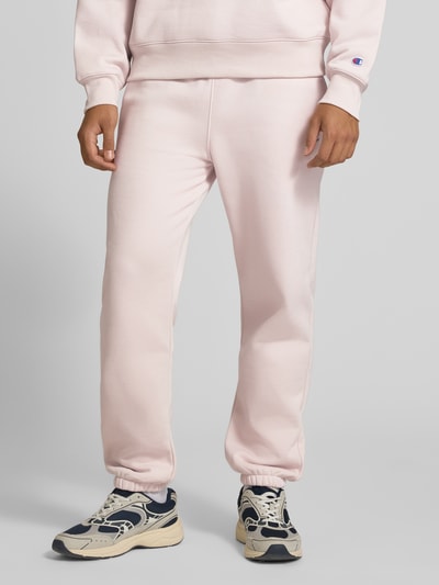 Männermodel trägt Sweatpants mit Label-Detail von Champion in Hellrosa, Baumwollmischung, gerader Schnitt, Nahaufnahme Unterkörper.