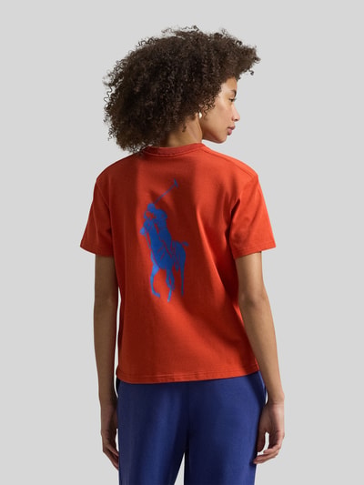 Frauenmodel trägt Regular Fit T-Shirt aus reiner Baumwolle von Polo Ralph Lauren in Unifarbe Orange mit blauem Motiv-Print, Ganzkörperansicht Rückansicht.