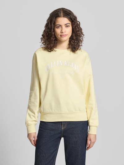 Frauenmodel trägt Sweatshirt mit Label-Print Modell 'GRAPHIC' von Calvin Klein Jeans in Pastellgelb, lockere Passform, Ganzkörperansicht von vorne.